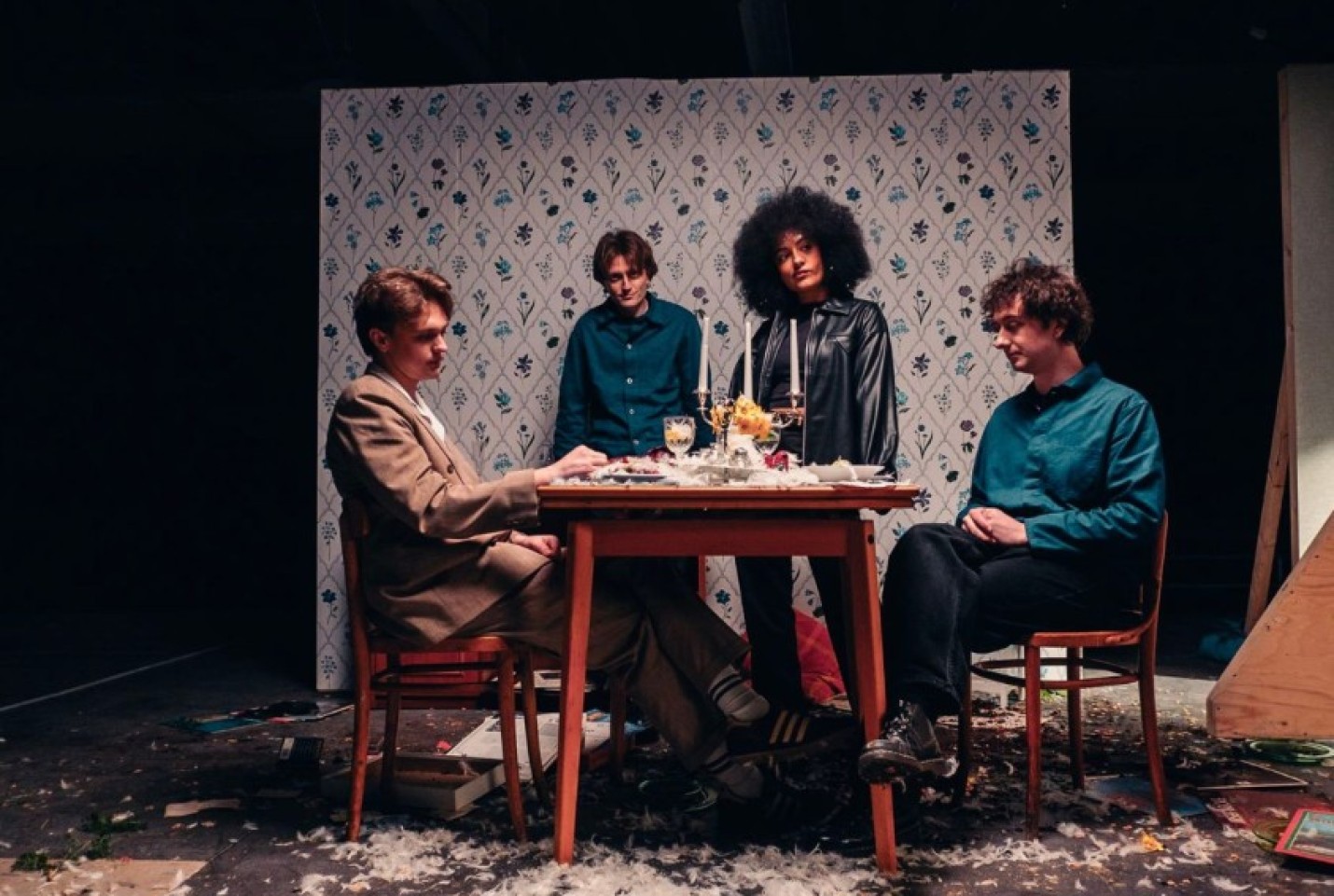 The band English Teacher, with members Lily Fontaine, Douglas Frost, Nicholas Eden and Lewis Witing all sat around a dining table with feathers around them.